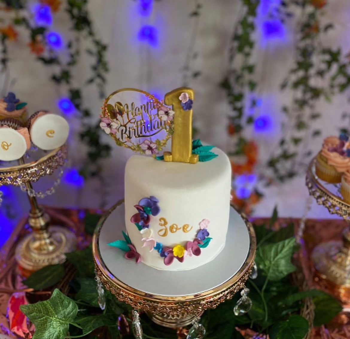 First birthday cake displayed on a decorated dessert table with '1' backdrop