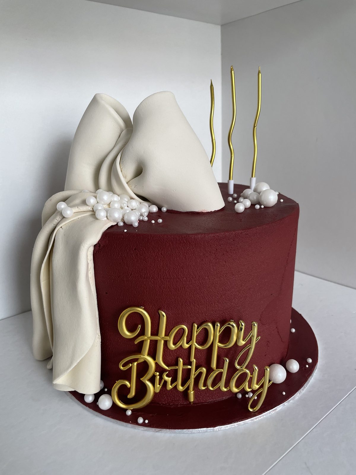 Burgundy cake with gold happy birthday topper and lit candles