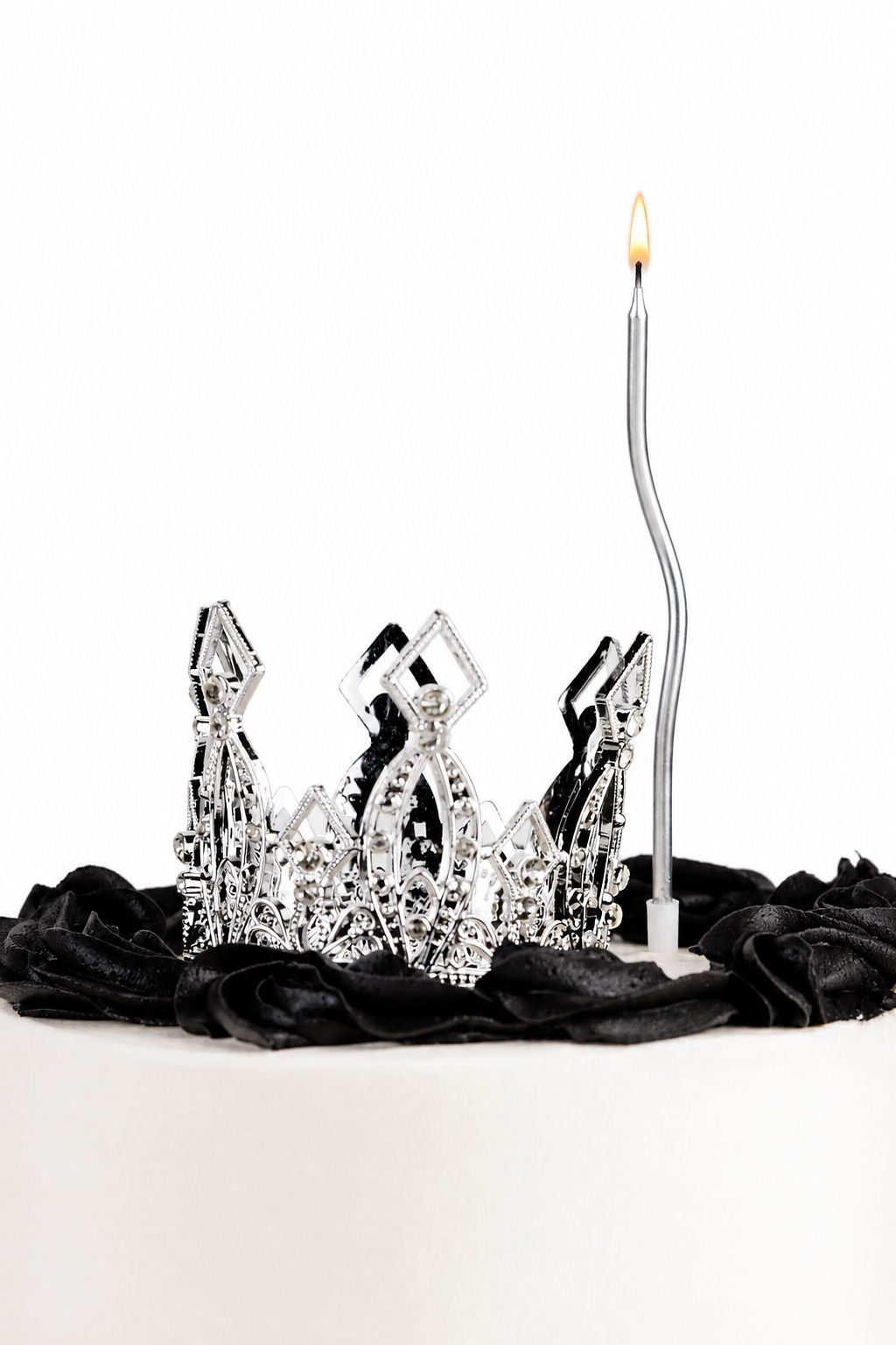 Black party cake with silver crown and lit sparkler candle