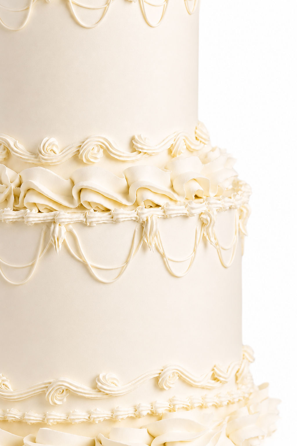 Ivory two-tier cake with intricate piped scrollwork and ruffled ribbon detail